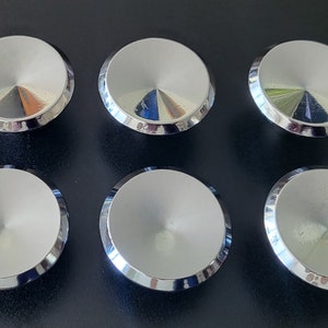 Peut inclure: Six boutons en métal de couleur argent avec un centre surélevé et arrondi. Les boutons ont une surface brillante et réfléchissante.