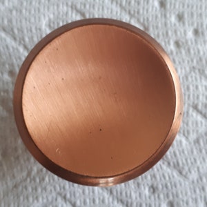 May include: A round, copper-coloured, metal disc with a smooth, slightly textured surface.