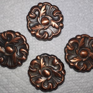 May include: Four antique bronze cabinet knobs with a floral design. Each knob features a central circular element surrounded by stylized leaves and swirling patterns. The knobs are arranged on a light grey surface.