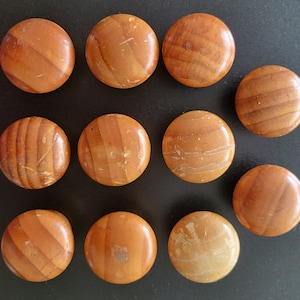 May include: Twelve round wooden knobs with a light brown wood grain pattern. The knobs have a smooth, polished finish.