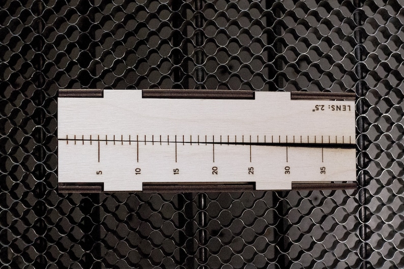 May include: A white wooden ruler with black markings and the text "LENS 25" printed on it. The ruler is marked in increments of 5, from 5 to 35.