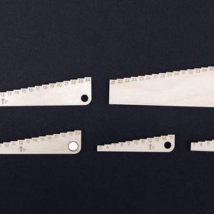 Pu&ograve; includere: Set di cinque righelli in legno con segni graduati per misurare diverse dimensioni. I righelli sono in legno marrone chiaro e hanno un foro all'estremit&agrave; per appenderli.