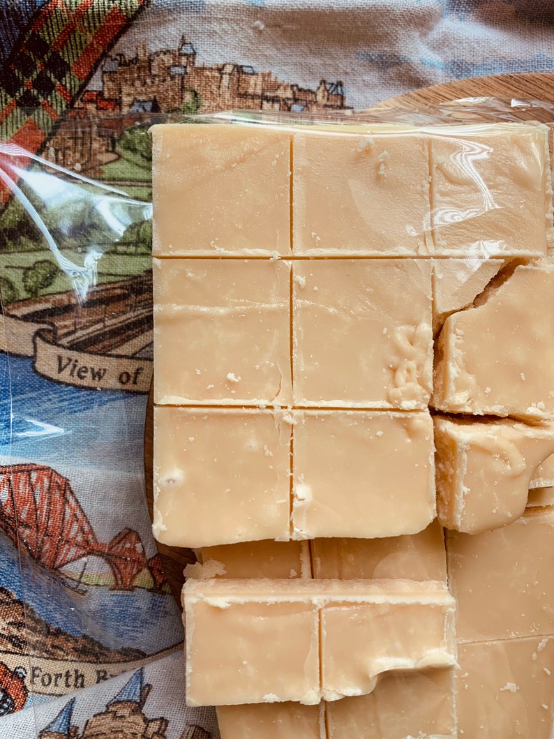 Może przedstawiać: Zbliżenie jasnobeżowych kwadrat&oacute;w fudge, niekt&oacute;re pocięte, a niekt&oacute;re połamane, w przezroczystym plastikowym opakowaniu. Tło przedstawia tkaninę z krajobrazem i napisem "View of Forth Bridge".