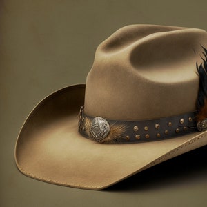 Könnte beinhalten: Ein brauner Cowboyhut aus Filz mit einem Lederband und einer silbernen Concho. Der Hut hat eine Feder an der Seite.
