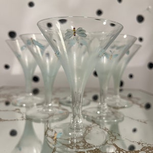 Puede incluir: Juego de cuatro copas de martini de vidrio transparente con acabado esmerilado y diseños de mariposas azules pintadas. Las copas tienen un tallo delicado y una copa ancha.