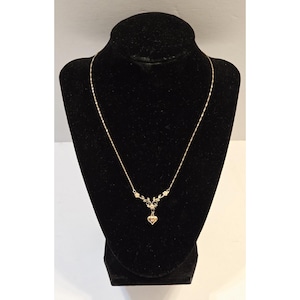 May include: A gold-toned necklace featuring a delicate chain and a central pendant design. The pendant consists of small metal leaves and floral accents, with a small heart-shaped charm suspended from the bottom center of the decorative piece.