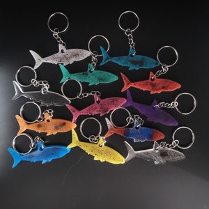 May include: A set of 12 colorful shark keychains with silver key rings. The sharks are made of a translucent material and are in various colors, including blue, green, orange, red, and purple.