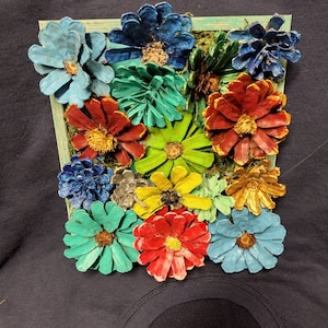 Puede incluir: Una pieza de arte de pared enmarcada que presenta una variedad de piñas pintadas en diferentes colores, incluidos el azul, el verde, el rojo, el amarillo y el dorado. Las piñas están dispuestas para parecerse a flores.