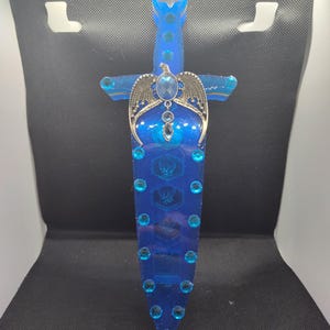 May include: A blue resin sword with a silver winged design and blue rhinestones. The sword is a decorative piece and is not sharp.
