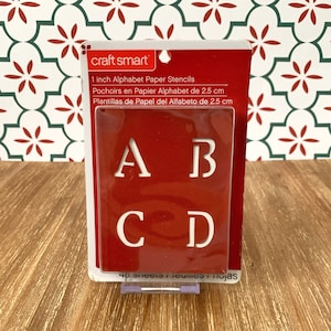 May include: A package of 40 1-inch alphabet paper stencils. The stencils are red and white and feature the letters A, B, C, and D. The package is labeled "craft smart" and includes the text "1 inch Alphabet Paper Stencils".