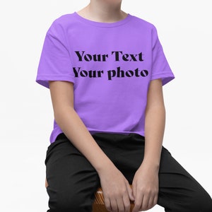 a young boy sitting on a chair wearing a purple t - shirt