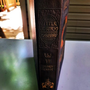 May include: A dark brown leather-bound book titled "Little Journeys" by Hubbard. The book is part of a series titled "Eminent Orators" and is volume VII.