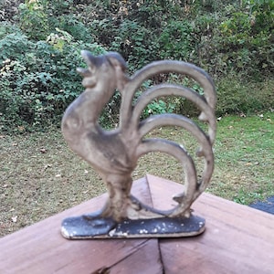 May include: A cast iron rooster bottle opener with a white painted finish. The rooster is standing on a base with its tail feathers curled up.