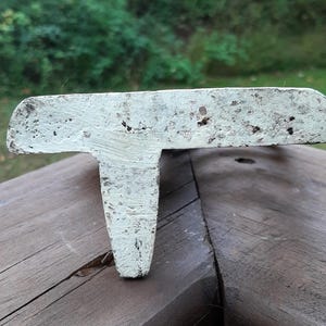 May include: White cast iron doorstop shaped like a T. The doorstop has a distressed finish and is sitting on a wooden surface.