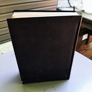 May include: A black leather-bound book with a brown bookmark sticking out of the top.