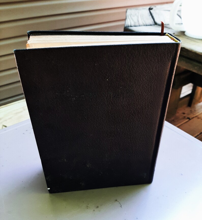 May include: A black leather-bound book with a brown bookmark sticking out of the top.