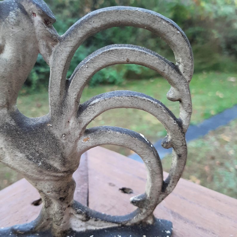 May include: Close-up of a cast iron rooster figurine with a detailed tail. The rooster is painted in a gray color with some white paint accents.