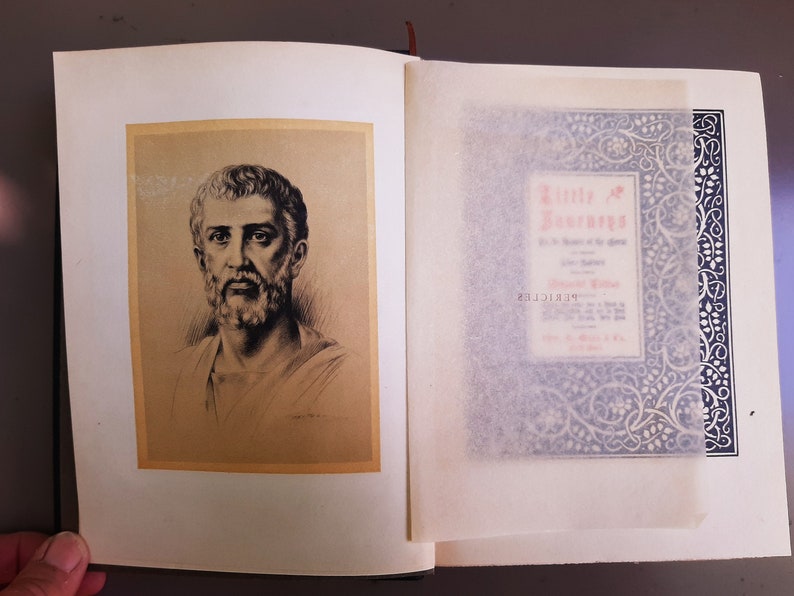 May include: A vintage book with a black and white illustration of a man with a beard on the front cover. The book's title is "Little Journeys" and is written in red and black text.
