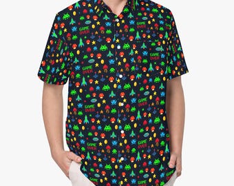 Pode incluir: Uma camisa de manga curta com botões em preto, apresentando um padrão colorido e repetitivo de ícones de videojogos pixelizados, incluindo foguetões, cogumelos, estrelas e o texto "GAME OVER" em verde e vermelho, com um bolso no peito esquerdo.