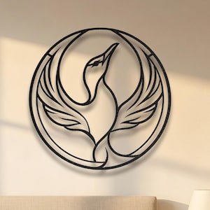 May include: A circular black metal wall art piece featuring a stylized phoenix with wings spread upward, enclosed within a thin circular frame. The design is composed of clean, continuous lines that form the silhouette of the mythical bird.