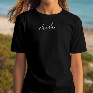 Könnte beinhalten: Ein schwarzes T-Shirt mit dem Wort "chechi" in weißer Kursivschrift auf der Vorderseite.