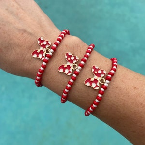 May include: Three red and white beaded bracelets with gold bow charms. Each charm has white polka dots on a red background.