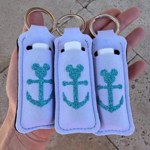 May include: Three white keychains with a teal glitter anchor and Mickey Mouse ears design. Each keychain has a clear tube for holding lip balm or other small items.