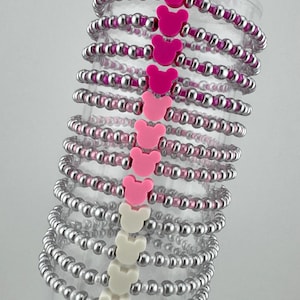 May include: A stack of silver and pink beaded bracelets with pink and white Mickey Mouse charms.