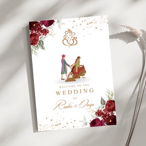 Könnte beinhalten: Eine weiße Hochzeits-Willkommenstafel mit einem Paar in traditioneller Kleidung, floralen Dekorationen und dem Text "Welcome to the Wedding of Ranbir & Divya". Das Design umfasst ein goldenes Ganesha-Symbol und burgunderfarbene Blumen.