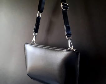 Può includere: Una borsa a tracolla in pelle nera con una lunga tracolla regolabile. La borsa ha una chiusura a zip e un design elegante e moderno.