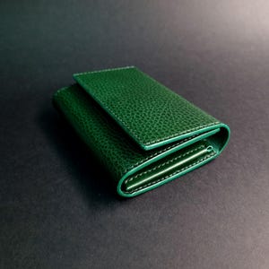 以下が含まれることがあります： 表面がテクスチャ加工された、折り畳まれた緑色の革の財布