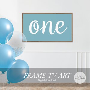 May include: A digital download of a printable frame art design featuring the word "one" in white cursive script on a light blue background. The frame is brown wood and the design is displayed on a white wall with blue balloons.