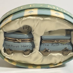 May include: A white ceramic mug with a black handle and the text "But First, Coffee" in a bold, black font. The mug is set against a blurred background, suggesting a cozy setting.