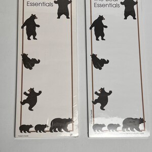 May include: Two identical rectangular notepads with white paper and brown borders. Each notepad features the text The Bear Essentials at the top and illustrations of black bears in various poses, including standing, sitting, and walking, arranged vertically.