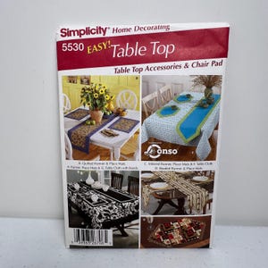 Op de afbeelding: Een Simplicity Home Decorating patroon voor tafelaccessoires en stoelkussens. De omslag toont afbeeldingen van tafellopers, placemats en tafelkleden in verschillende ontwerpen en kleuren. Het patroonnummer is 5530.