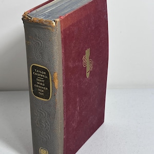 May include: A hardcover book with a burgundy cover and a gray spine. The spine features gold lettering and the title "Taylor Caldwell". The book's cover has a gold emblem. The book's edges show signs of wear.