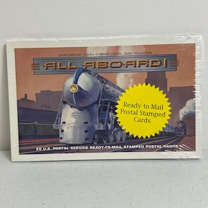 Puede incluir: Un paquete sellado de postales timbradas de Trenes del siglo XX. La parte frontal del paquete presenta una ilustración de tren vintage con las palabras "ALL ABOARD!" y una etiqueta amarilla que dice "Ready to Mail Postal Stamped Cards".