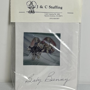 May include: A package featuring a printed image of two stuffed bunny rabbits. The bunnies are wearing patterned clothing. The package is labeled "J & C Stuffing" and "Baby Bunny".