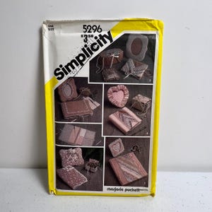May include: A Simplicity sewing pattern envelope with a yellow border. The pattern features various fabric crafts, including heart-shaped and rectangular decorative items. The envelope displays the Simplicity logo and the number 5296.