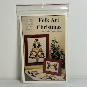 May include: A Folk Art Christmas craft kit by Cindy Taylor Oates. The package features a design of a Christmas tree and angels. The kit includes a variety of colors, including red, green, and beige. The package is sealed in a clear plastic bag.