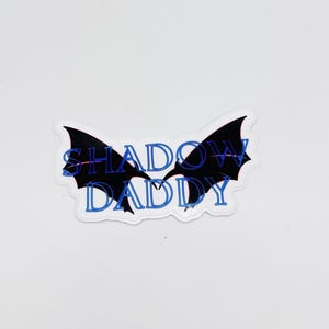 May include: Black and white sticker with a pair of wings and the text "SHADOW DADDY" in blue.
