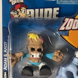 Pode incluir: Um conjunto de skate Tech Deck Dude Zoods com uma figura de aparência de zumbi com uma camisa azul e uma figura de cachorro branco. O conjunto inclui um skate vermelho com rodas pretas. A embalagem é azul e apresenta o logotipo Tech Deck e as palavras "Dude Zoods".