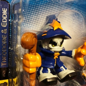 May include: A blue and white wizard action figure with a staff. The figure wears a blue hat with a gold star, a blue coat, and white boots. The figure is in a clear plastic package. The text "Theodore & Eddie" is visible.