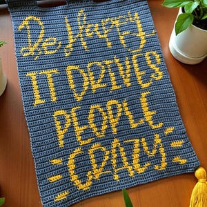 Peut inclure: Une tenture murale en crochet bleu avec l'inscription jaune "Be Happy It Drives People Crazy". Elle est ornée d'une barre de suspension noire et de pompons jaunes. Décoration intérieure faite à la main.