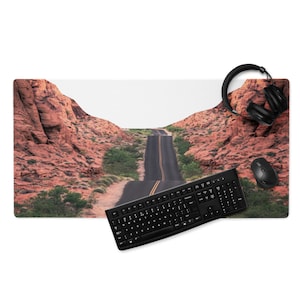May include: A black keyboard and mouse are placed on a red rock desert landscape mousepad. The mousepad features a winding road through the desert.
