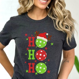 May include: A dark grey t-shirt with a Christmas-themed design featuring the word "HO HO HO" with a red and green polka dot ball for each "O". The top "O" has a Santa hat on it.