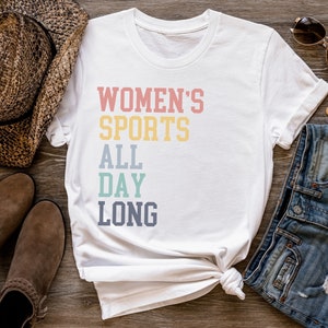 May include: White t-shirt with the text "WOMEN'S SPORTS ALL DAY LONG" in a rainbow color scheme.