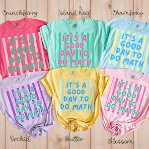 May include: Five short-sleeved t-shirts in various colors including pink, mint green, light blue, lavender, and yellow. Each shirt features vertical stripes and the text "IT'S A GOOD DAY TO DO MATH" printed in a contrasting color on the front.