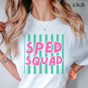 May include: A white t-shirt featuring a graphic design with vertical mint green stripes and the text SPED SQUAD printed in bold, rounded pink letters across the center. The word White is printed in the top right corner of the image.