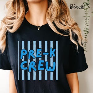 May include: Black t-shirt featuring the text "PRE-K CREW" in blue, with a white outline, set against a backdrop of vertical blue stripes. The word "Black" is written in cursive in the top right corner.